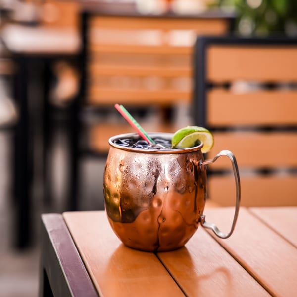 A Moscow Mule in a copper mug with a lime wedge and straw on a wooden table.