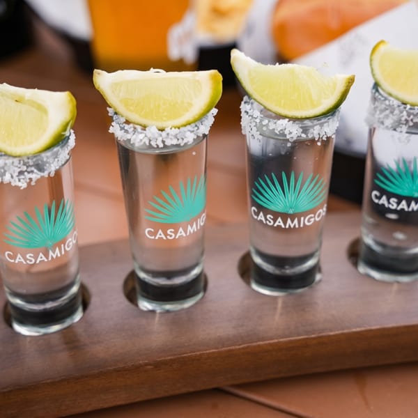 Four Casamigos tequila shots with salt rims and lime wedges on a wooden tray.
