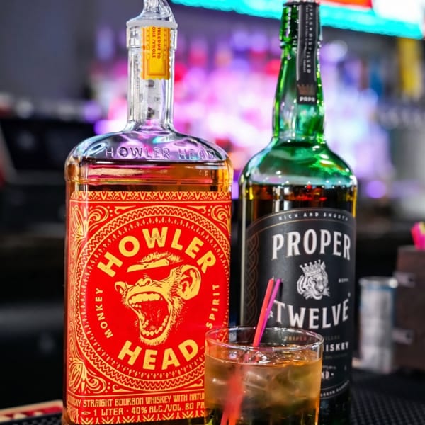 Two whiskey bottles, Howler Head and Proper Twelve, with a glass of whiskey and ice.
