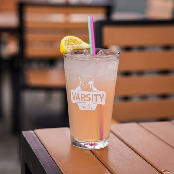 A Varsity Ice House branded drink with a lemon slice and colorful straws on a wooden table.