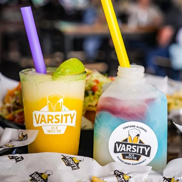 Two Varsity Ice House drinks, one yellow with lime and one blue/pink, with fries and tacos.